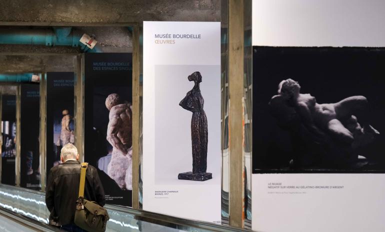 6 panneaux d&#039;expositions qui représentent des sculptures du Musée Bourdelle, positionnés le long d&#039;un tapis roulant sur lequel se trouve un homme avec un sac sur l&#039;épaule.